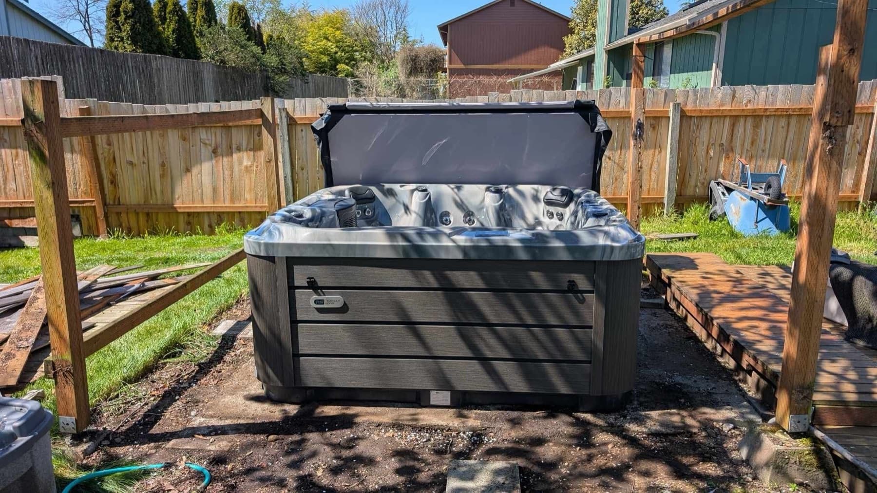 Hot tub with cover lifter beside a wood fence