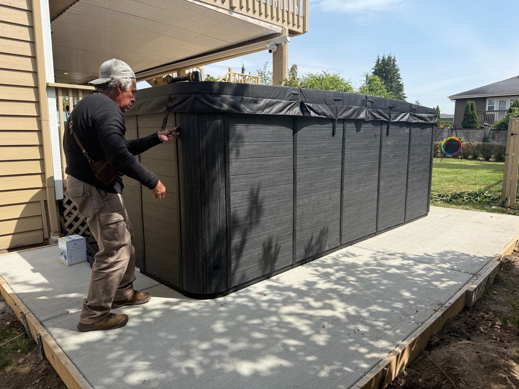 Delivery crew moving a wrapped hot tub onto a concrete pad