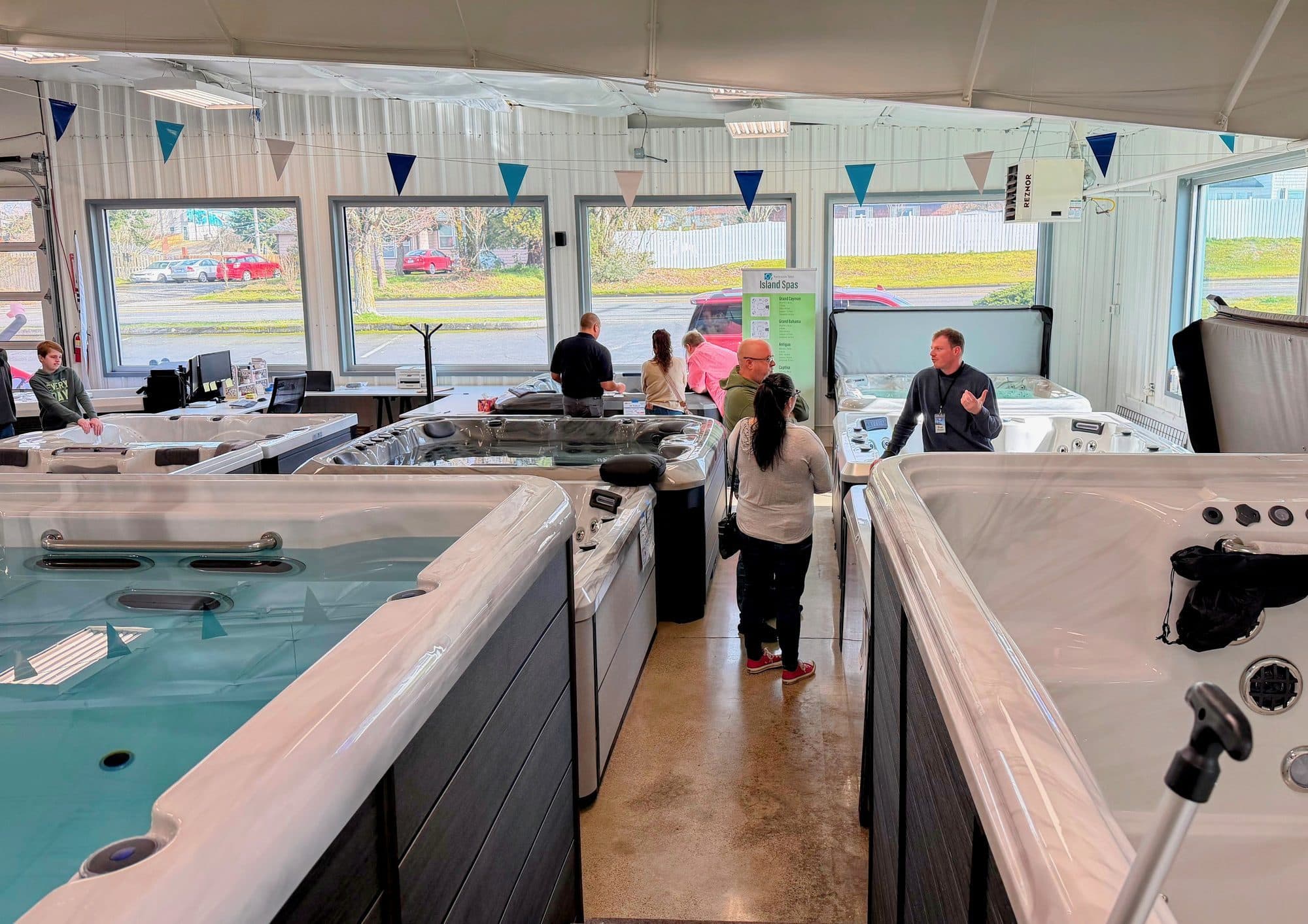 Customers talking with Black Pine staff between filled hot tubs and swim spas on the Tacoma showroom floor